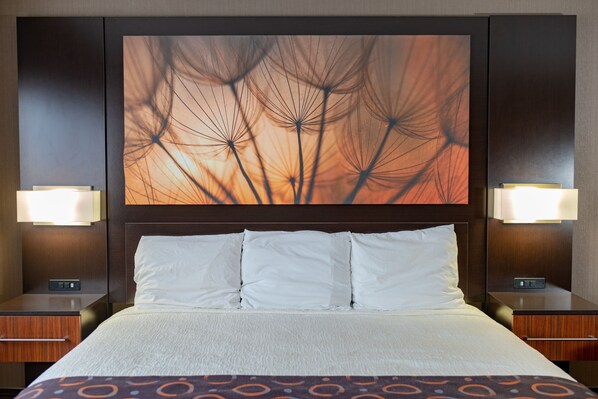 Habitación de hotel con una cama grande, dos mesitas de noche y una obra de arte en la pared de semillas de diente de león.