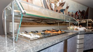 Uma área de buffet com estrutura de vidro, bandejas de servir e um mural ao fundo.