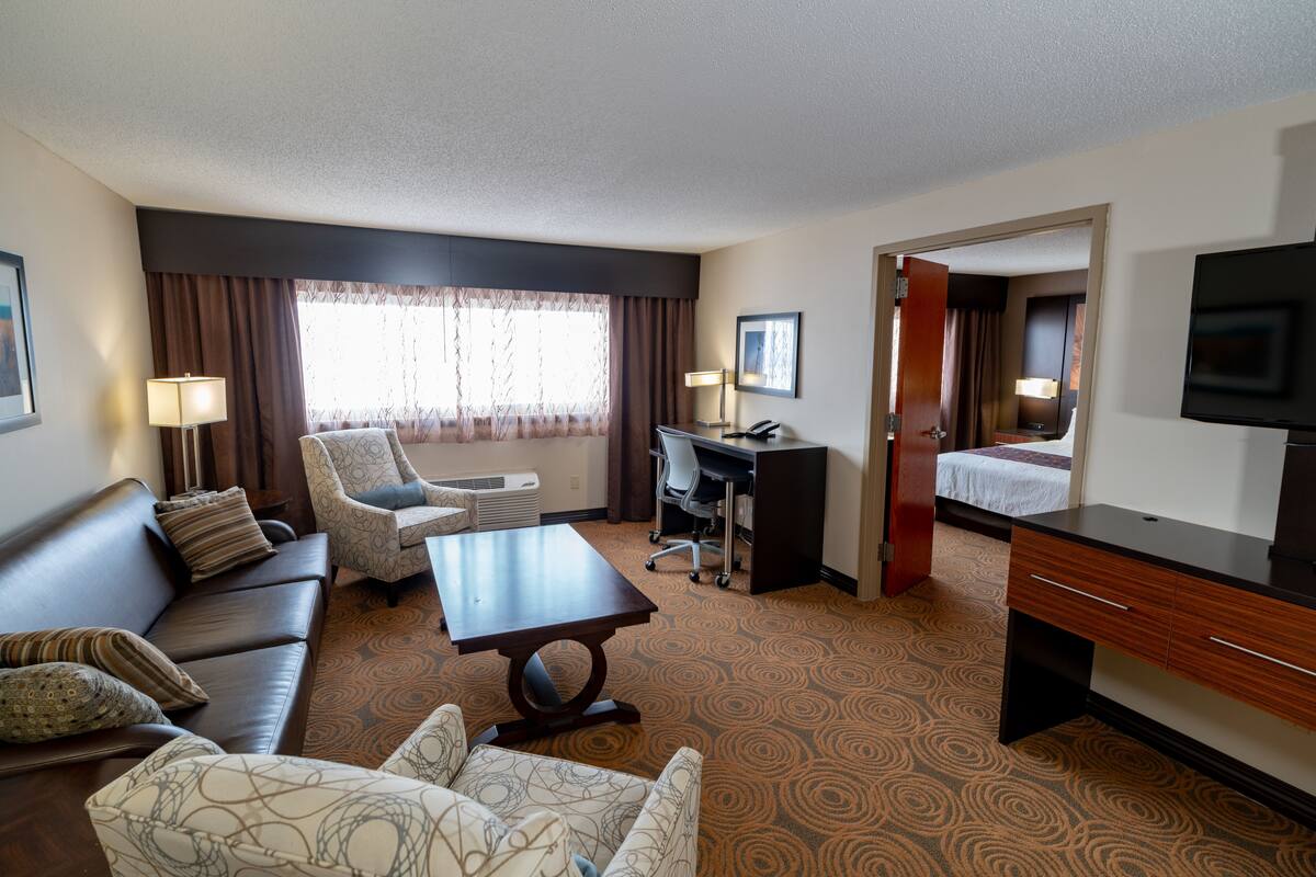 A hotel room with a sofa, armchair, desk, and a television.