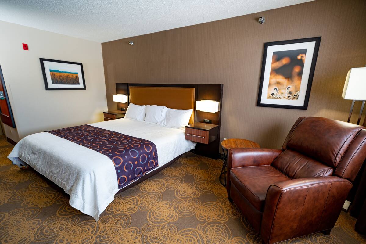 A hotel room with a large bed, a brown leather chair, and two wall-mounted lamps.