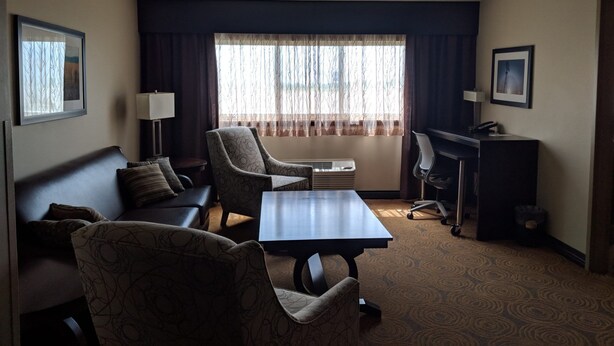 A hotel room with a sofa, armchair, desk, and a large window with curtains. - Royal River Casino and Hotel (Flandreau)