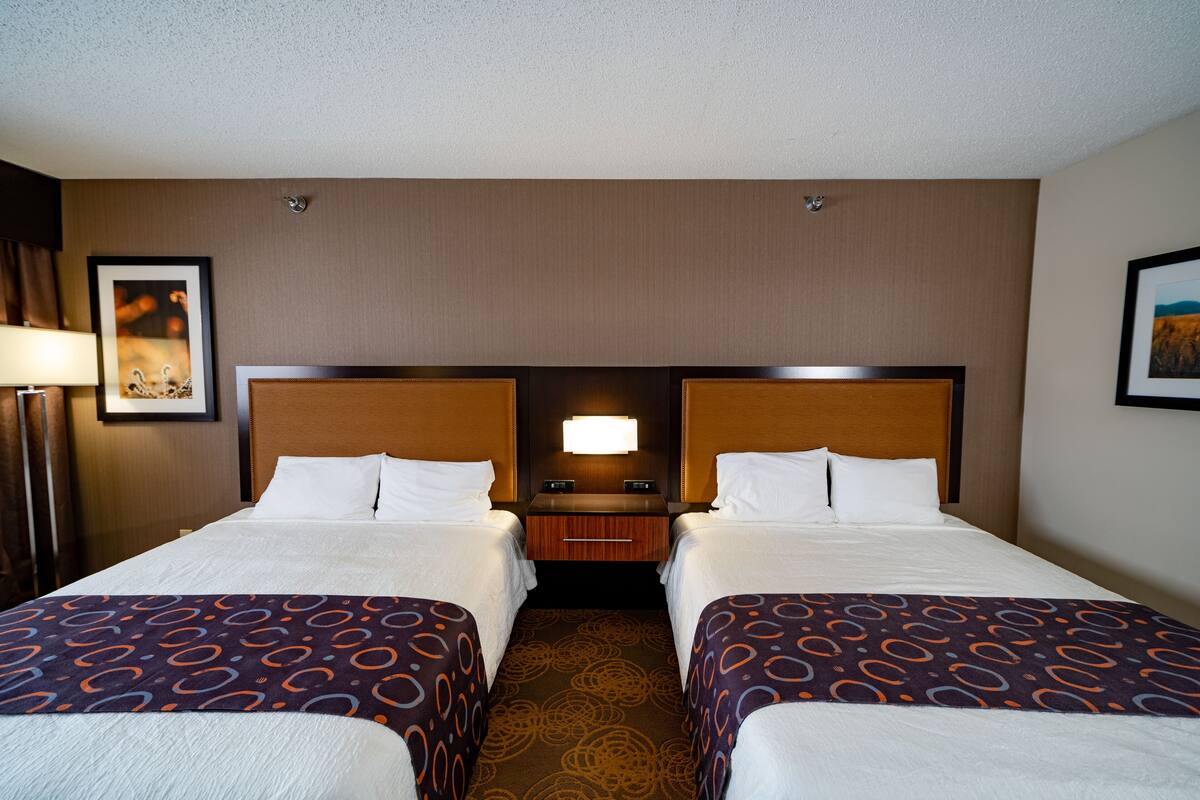 A hotel room with two beds, a nightstand, and a wall-mounted lamp.