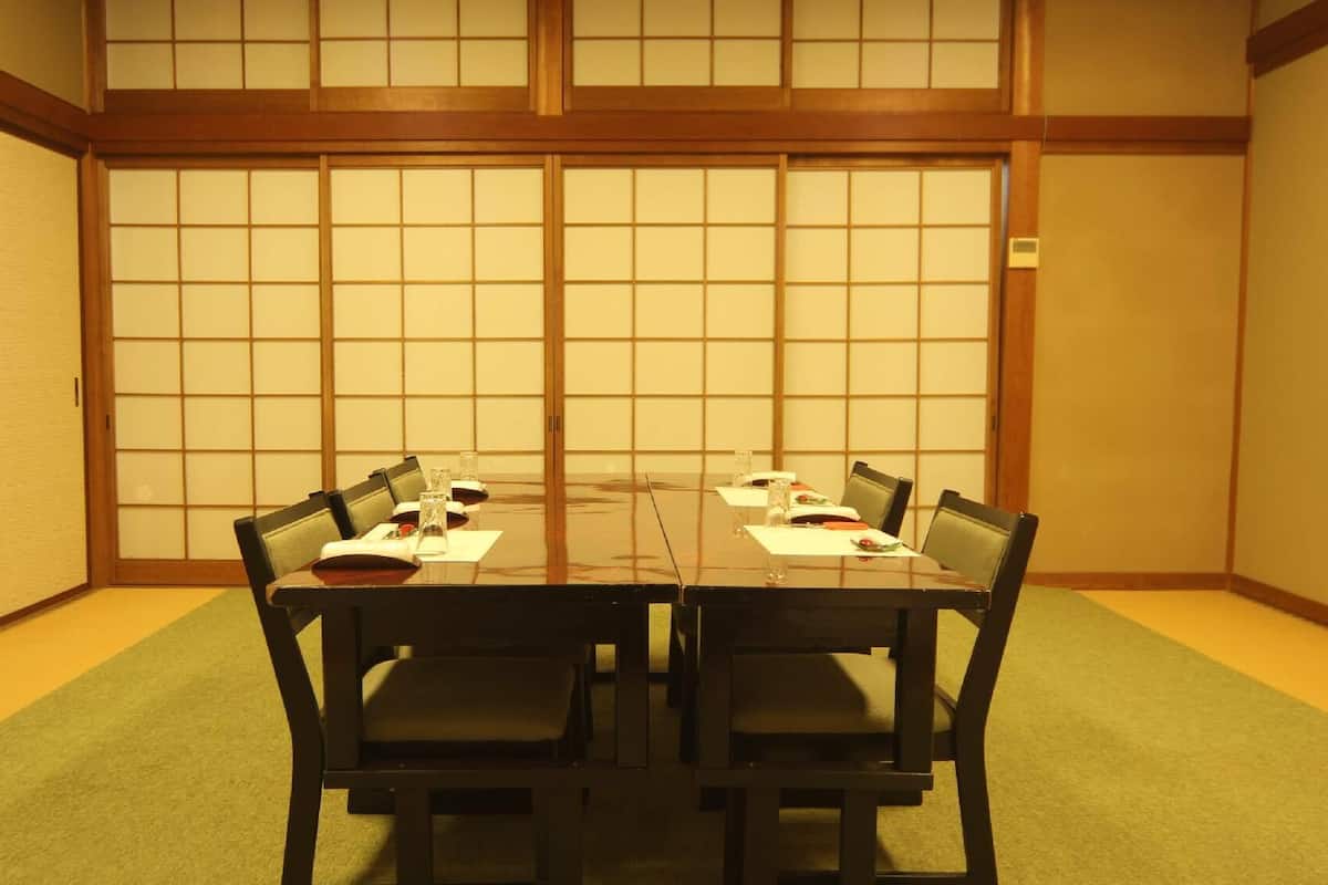 Ein traditioneller japanischer Raum mit Tatami-Bodenbelag, einem niedrigen Tisch mit Stühlen und Shoji-Schiebetüren.