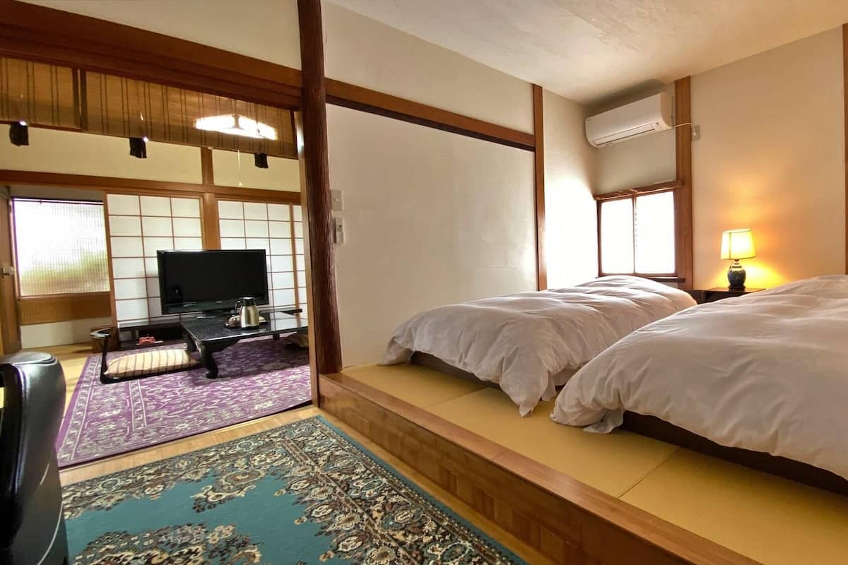 Ein traditioneller japanischer Raum mit Tatami-Böden, einem Fernseher und einem Bett mit weißer Bettwäsche.
