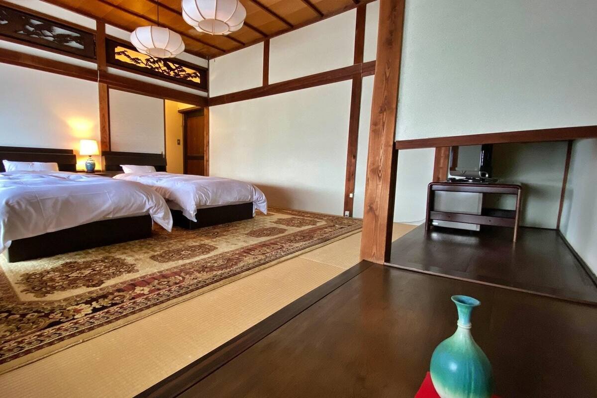 Ein traditioneller japanischer Raum mit zwei Betten, einem Tatami-Boden, einem Holztisch und einer Ziervase.