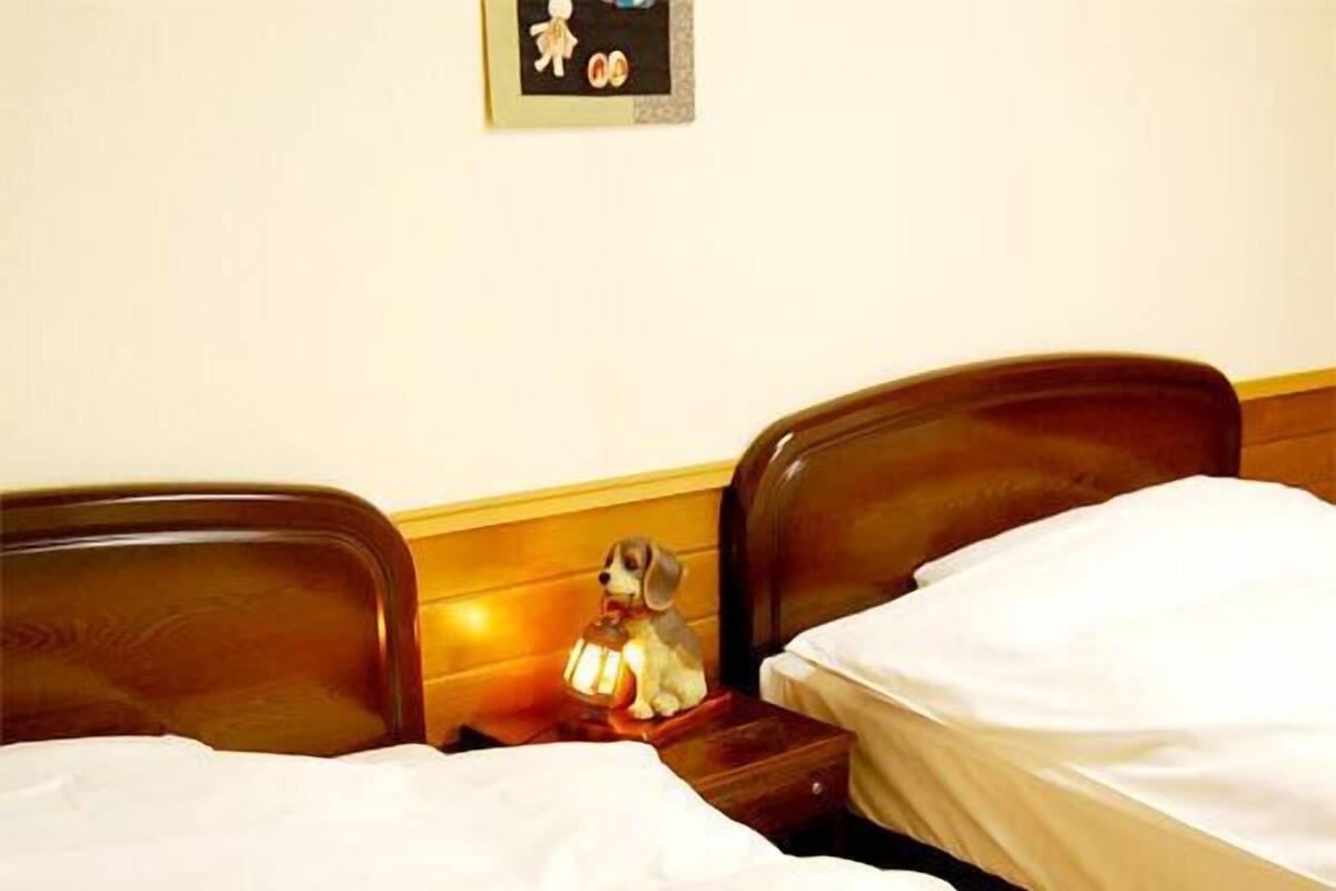 Una habitación de hotel con dos camas, una mesita de noche con lámpara y un reloj de pared.