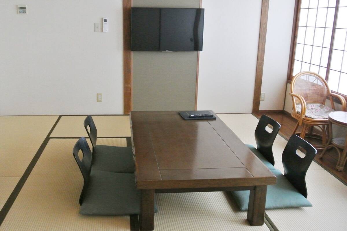 Una habitación japonesa tradicional con suelo de tatami, una mesa baja y un televisor montado en la pared.