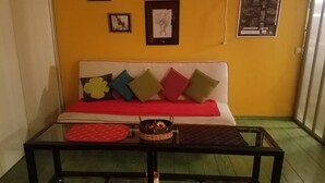 Ein Zimmer mit einer gelben Wand, einem weißen Sofa mit bunten Kissen und einem Glastisch mit einem Korb und einer roten Unterlage.