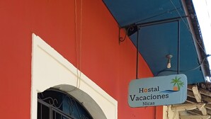 Un edificio con fachada roja, una puerta azul con barrotes de metal y un letrero que indica 'Hostal Vacaciones Nicas'.