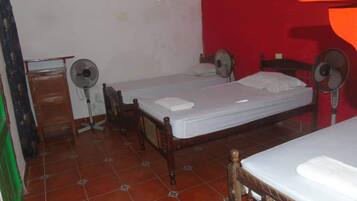A room with two single beds, a wooden dresser, and two standing fans.