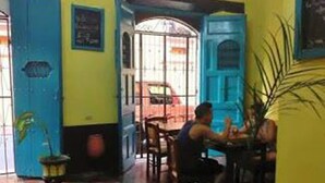 Un interior de restaurante con suelo a cuadros, una puerta azul y una persona sentada en una mesa.