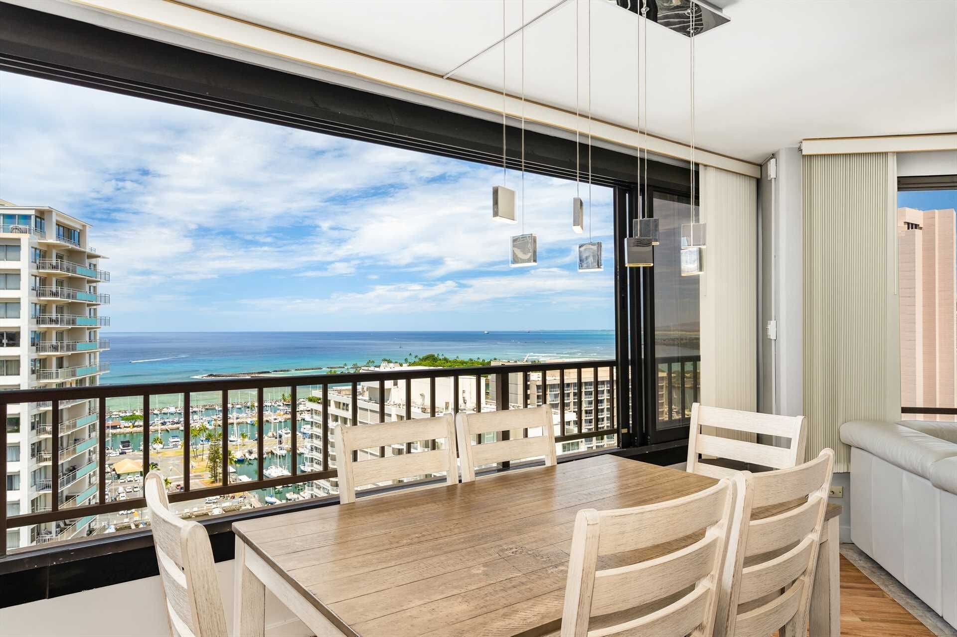 Un balcón con mesa y sillas de madera, con vista a un puerto deportivo y al océano.