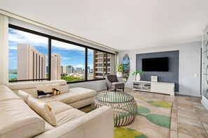 A modern living room with a large window, a sofa, a coffee table, a chair, a TV, and a small side table.