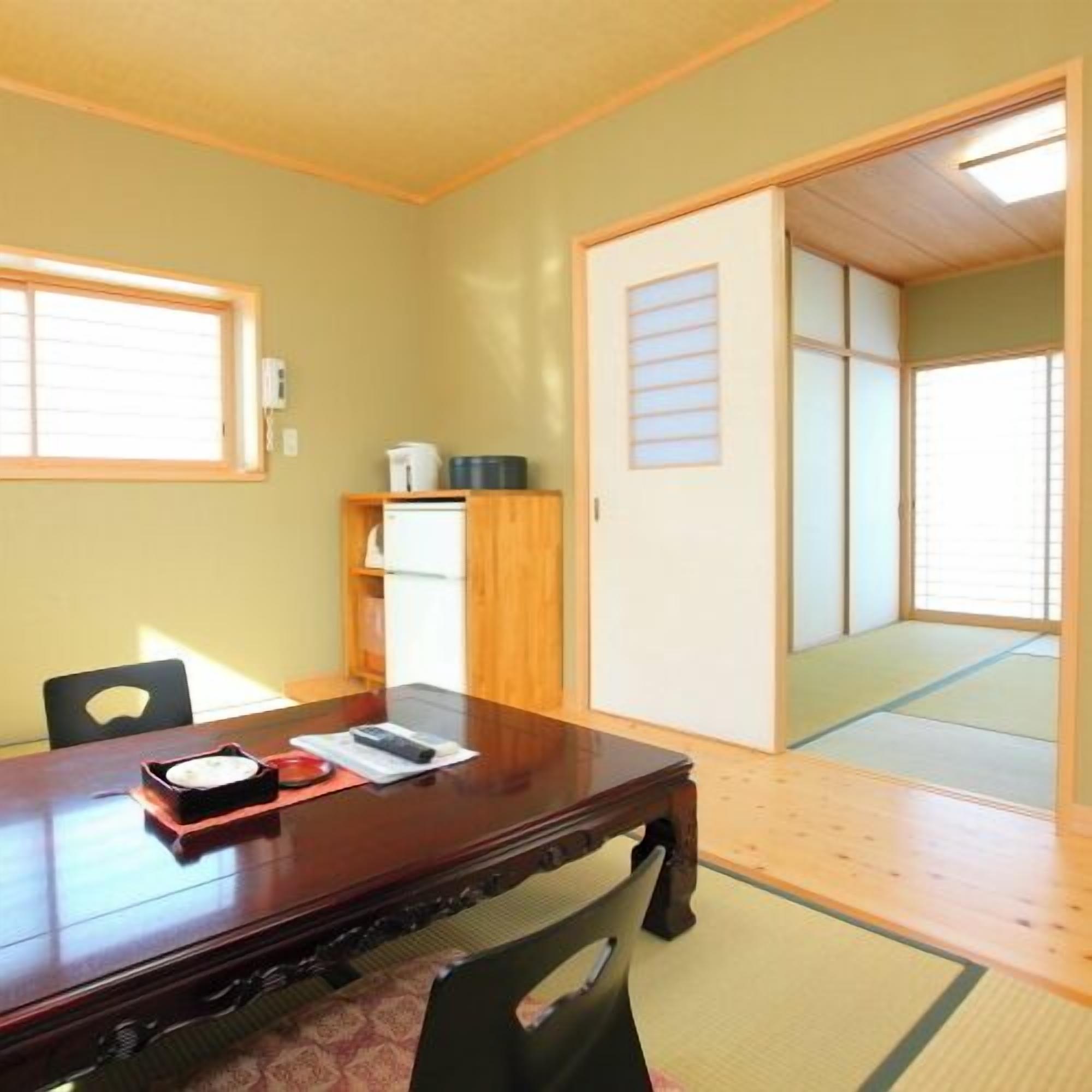 A traditional Japanese room with tatami flooring, a wooden table, a refrigerator, and a sliding door.