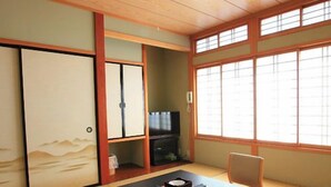 A traditional Japanese room with tatami flooring, a low table with a cushion, a television, and sliding doors. - Yumigahama Ichibankan (Minamiizu)
