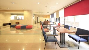 Ett rymligt inomhusområde med sittplatser, en receptionsdisk och stora fönster.