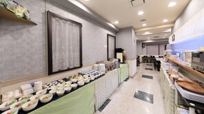 Montaje de bufé con diversos alimentos y una larga mesa cubierta con mantel verde.