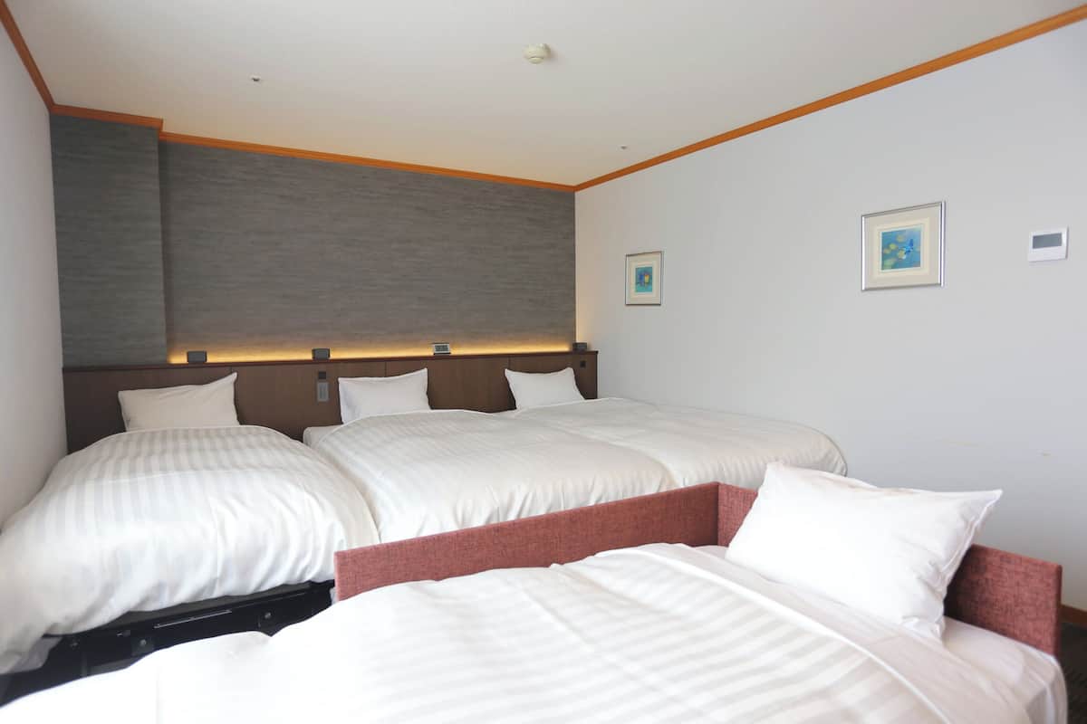 A hotel room with a large bed, a headboard with built-in lighting, and two framed pictures on the wall.