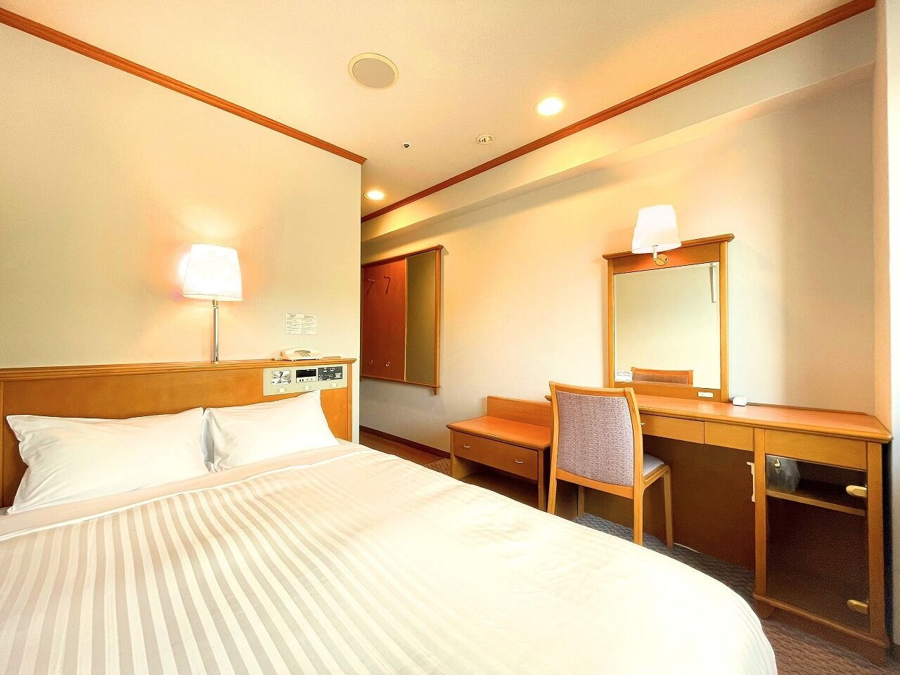 Une chambre d’hôtel avec un lit, un bureau, une chaise, un miroir et une lampe.