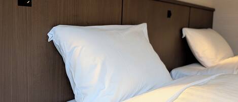 A neatly made bed with white bedding and pillows, a wooden headboard, and a small illuminated panel on the wall.