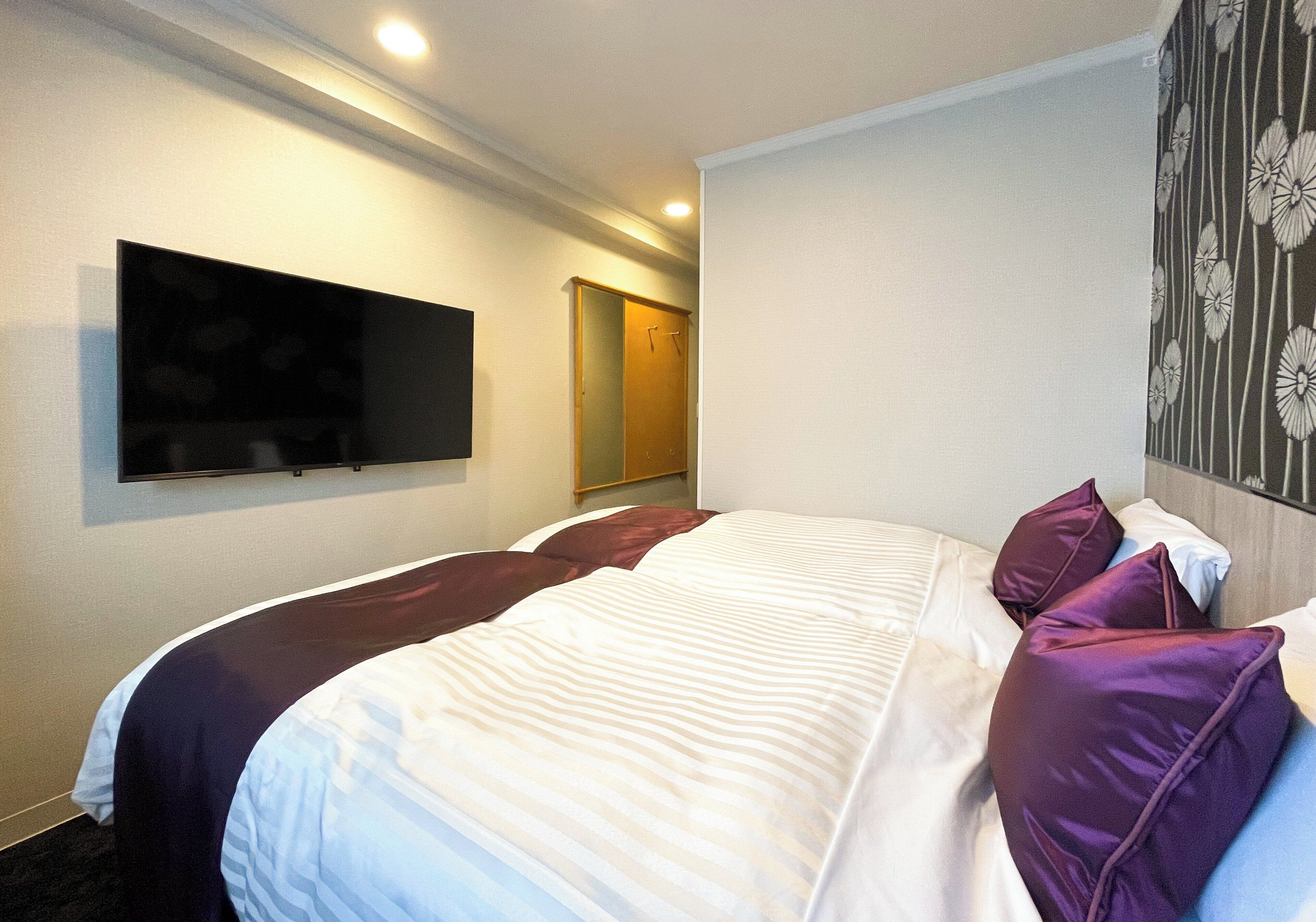 A hotel room with a bed, a television on the wall, and a door leading to another room.