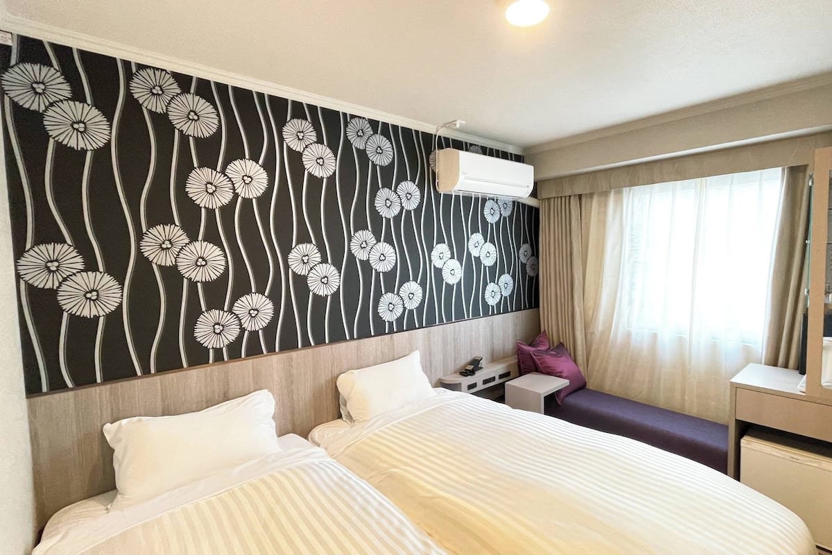A hotel room with a bed, bedside table, and a wall with a floral pattern.
