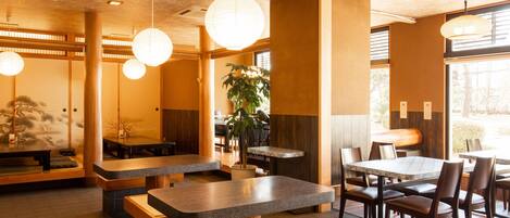 A restaurant interior with wooden tables and benches, hanging paper lanterns, and a large window providing natural light.
