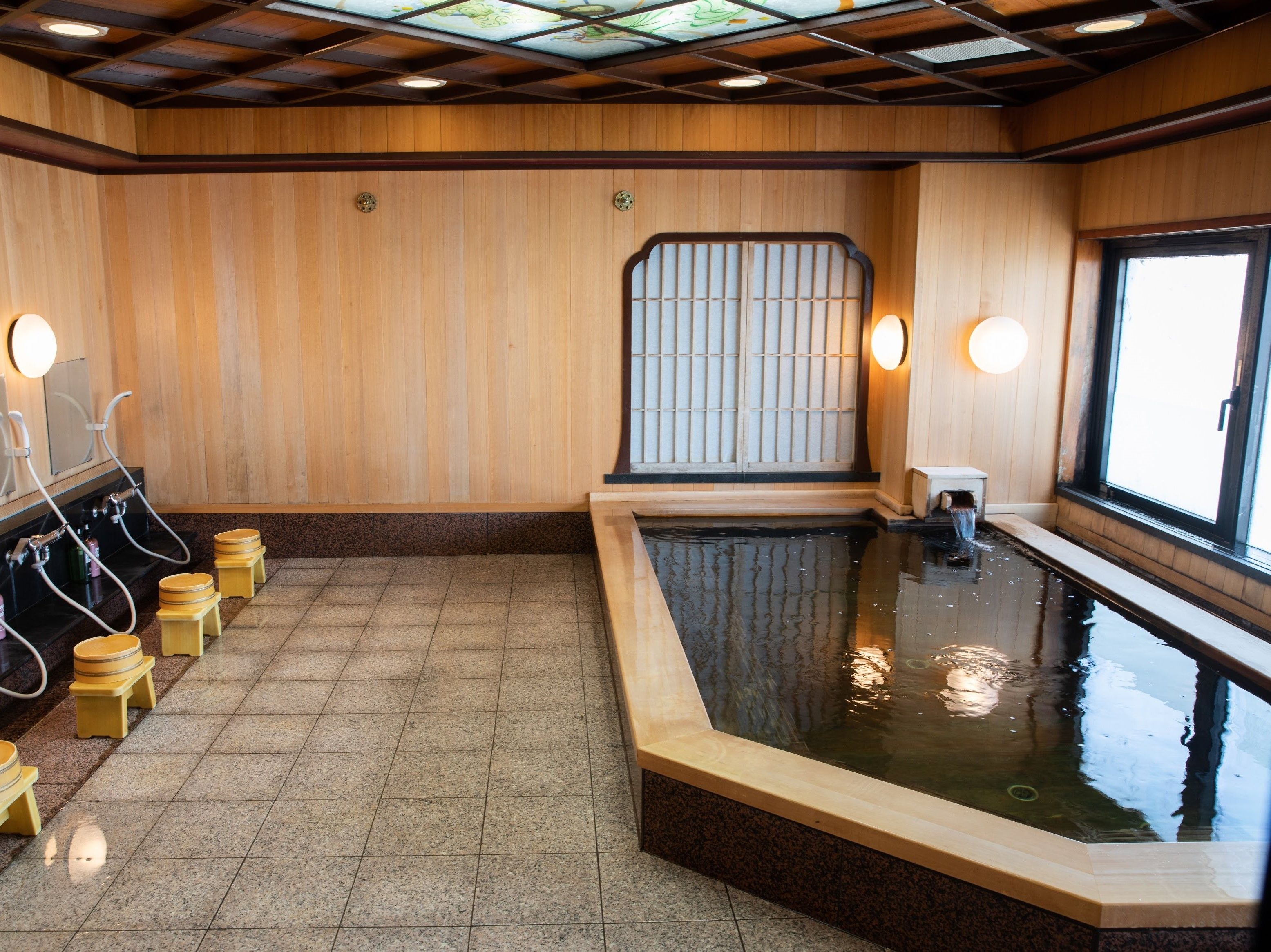 A traditional Japanese onsen with wooden walls, a stone floor, and a small pool.