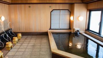 Un onsen japonés tradicional con paredes de madera, suelo de piedra y una pequeña piscina.