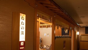 Un intérieur japonais traditionnel avec un comptoir d’accueil en bois, un panneau indiquant un espace réservé aux femmes, et une pièce avec des tatamis visible à travers une porte ouverte.