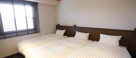 Un lit double avec une tête de lit en bois, une fenêtre avec des stores et un sol recouvert de moquette.