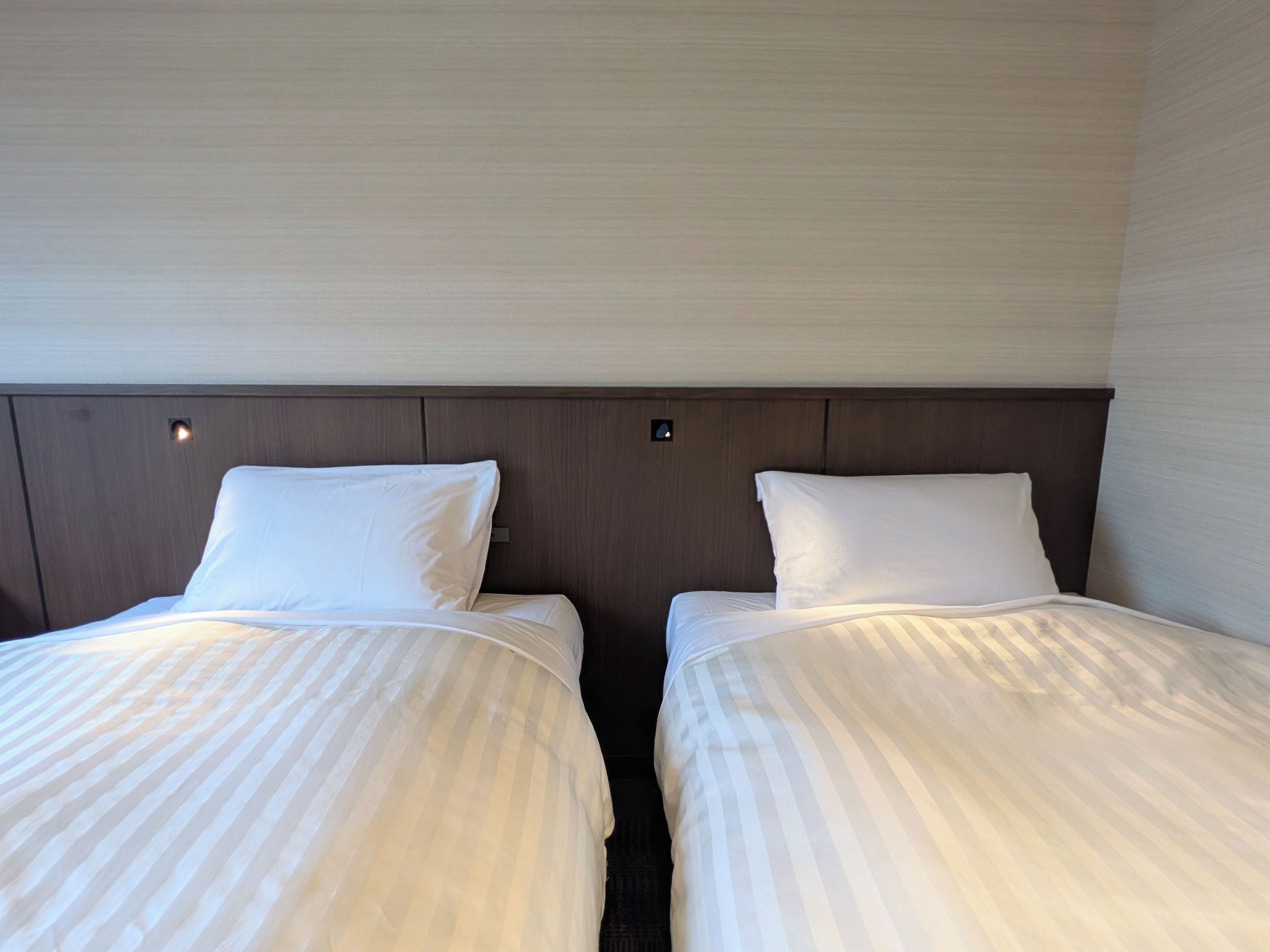 A hotel room with two beds, each with a headboard and pillows.