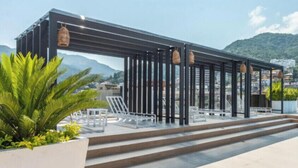 Een terras op het dak met een pergola, buitenmeubilair en uitzicht op de stad en bergen.