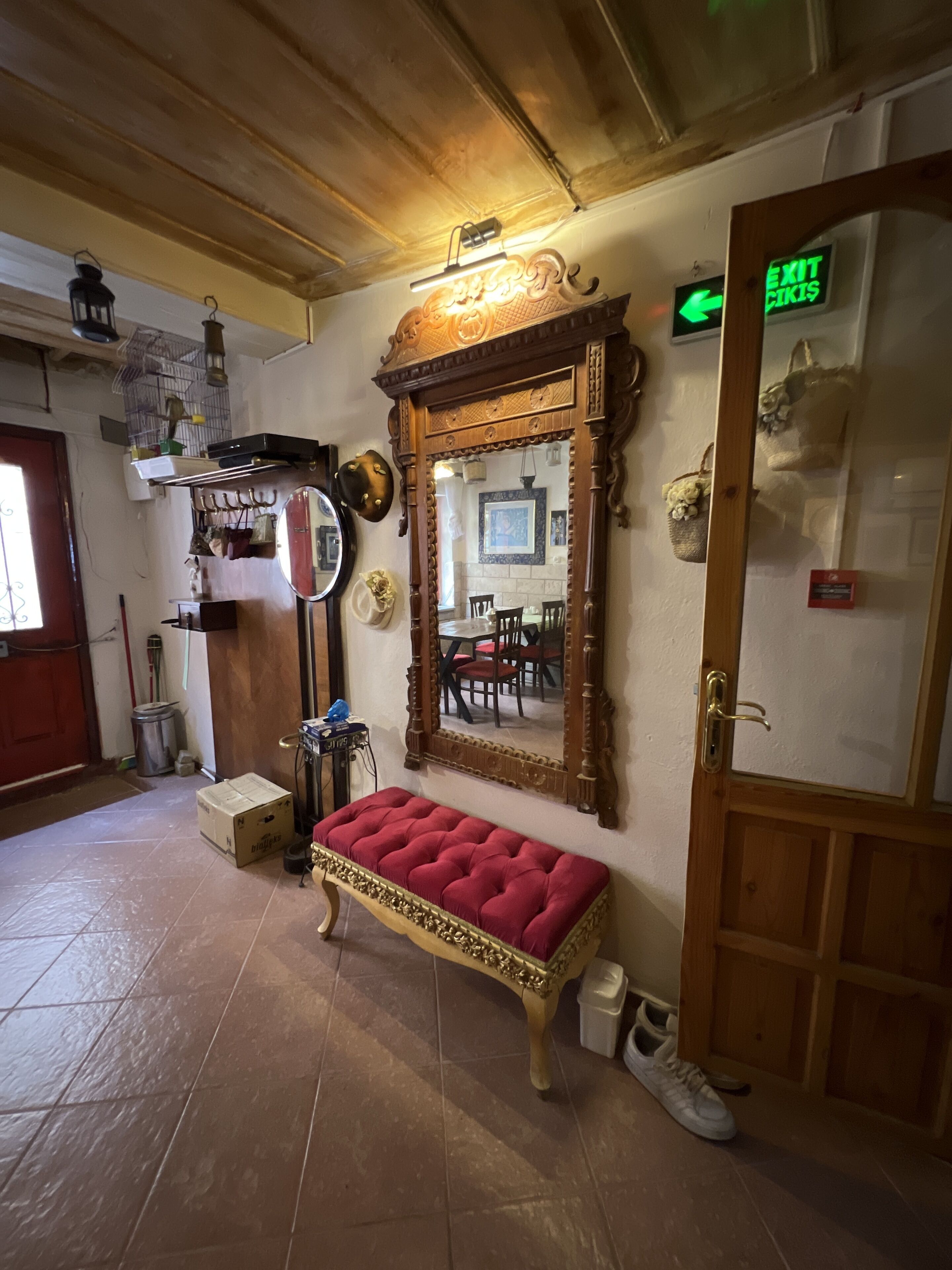A room with a wooden bench, a large mirror, a door with an exit sign, and a tiled floor.