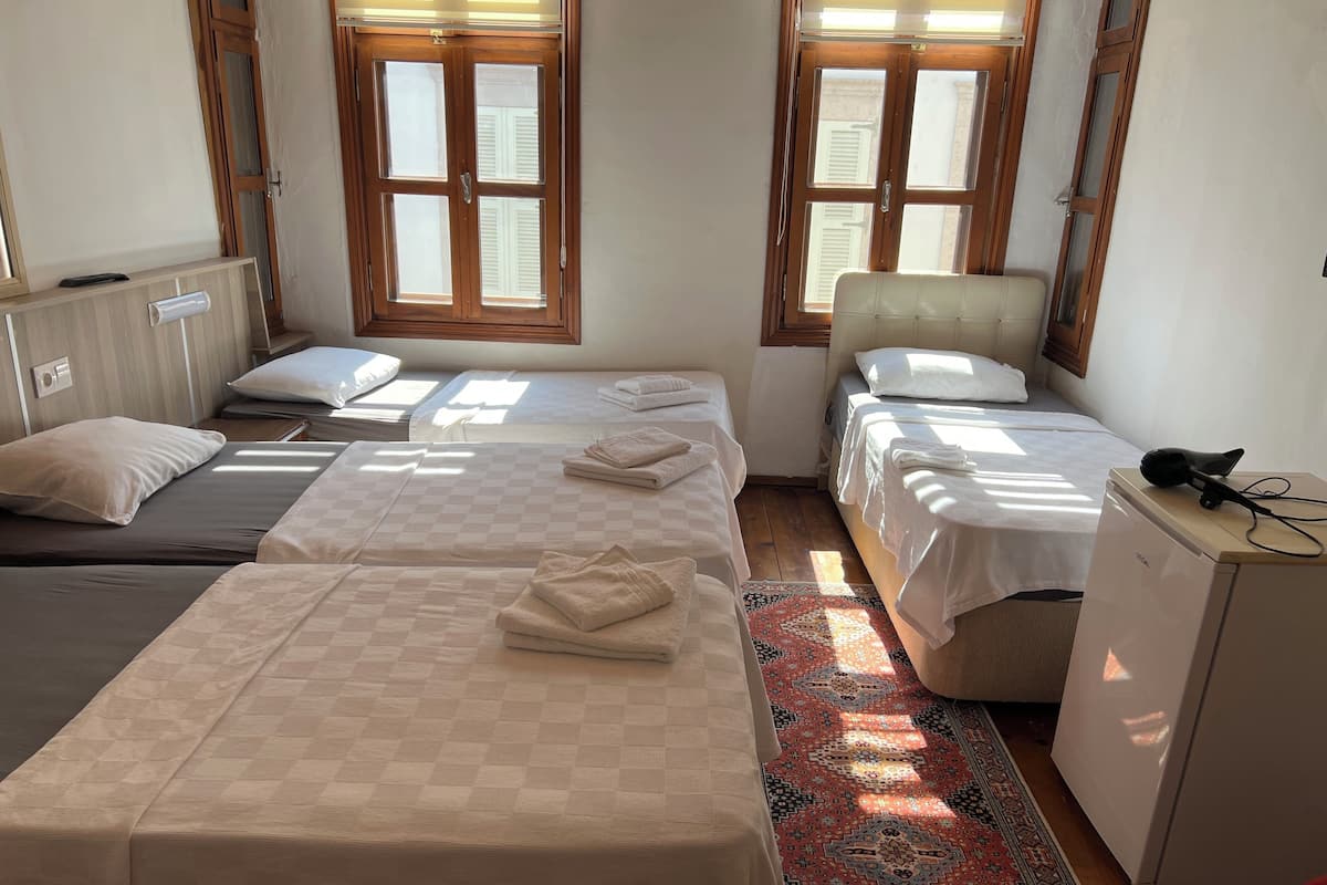 Une chambre d’hôtel avec deux lits simples, un petit bureau, une chaise, un radiateur et une fenêtre avec des volets.