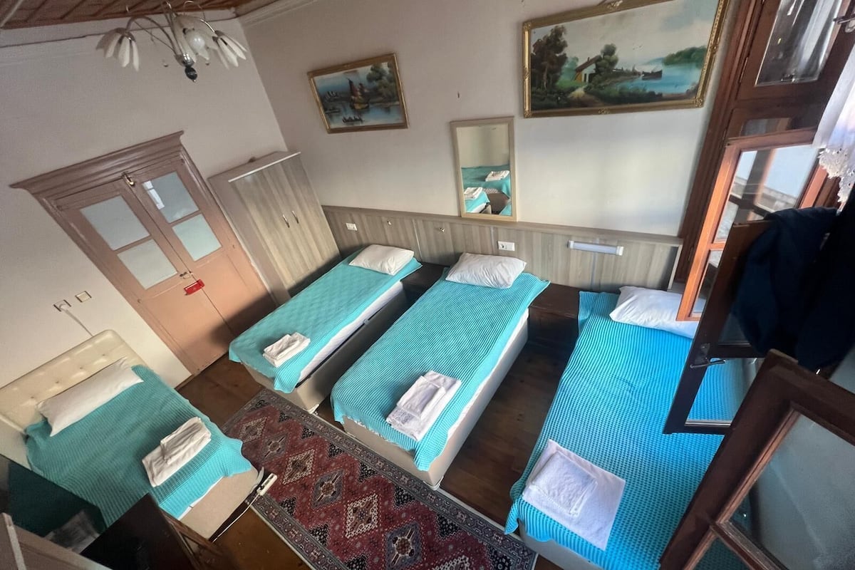 Une chambre avec trois lits simples, une armoire en bois, un miroir et un tableau accroché au mur.