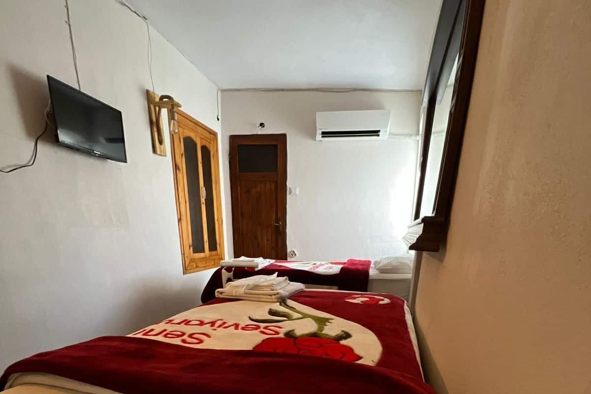 Une chambre d’hôtel étroite, avec deux lits, un téléviseur, une porte en bois et un appareil de climatisation.