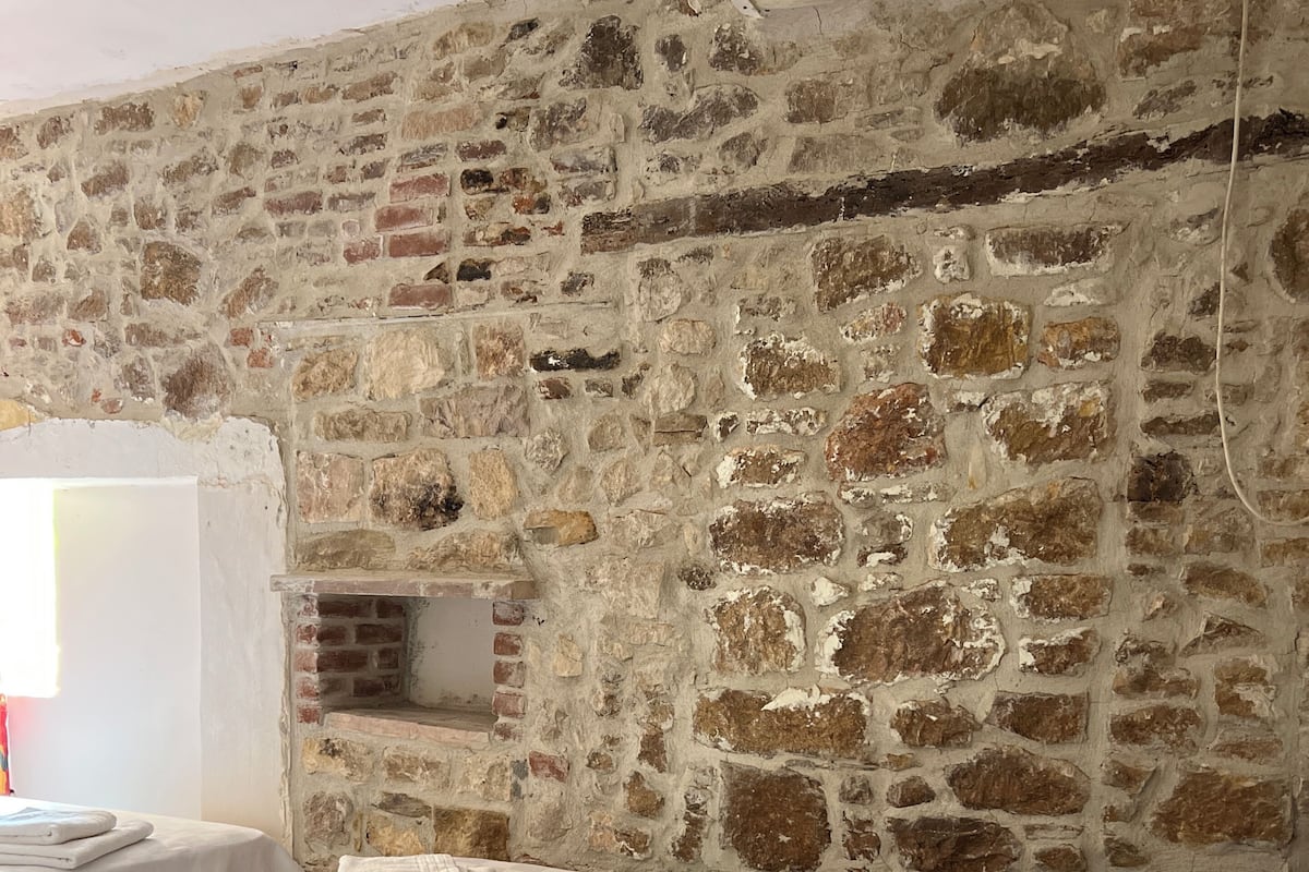 Une pièce avec un mur en pierre, un lit avec une literie blanche, une table de chevet et une petite table de nuit en bois.
