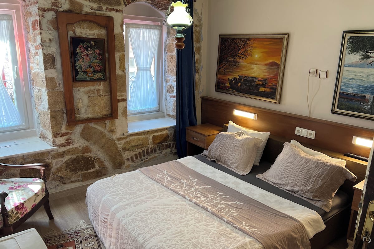 Une chambre confortable avec un grand lit, une table de chevet, une fenêtre avec des rideaux et un tableau au mur.