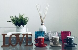 Una mesa con objetos decorativos, incluyendo una planta en maceta, difusor de aroma y tazas de varios colores.