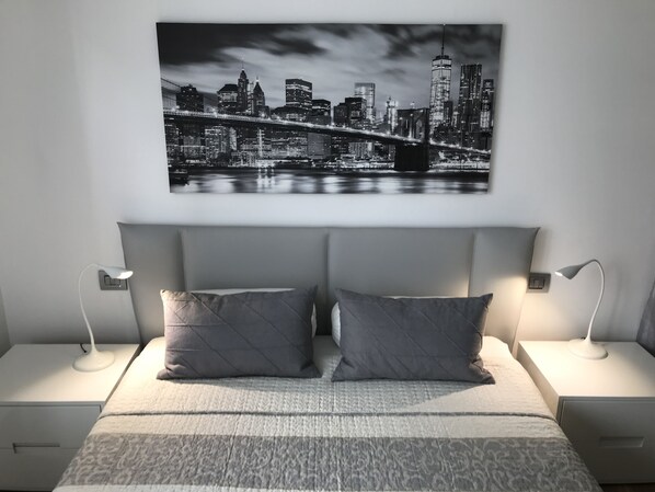 Un dormitorio con vista a la ciudad, dos mesitas de noche con lámparas y una cama con colcha estampada.