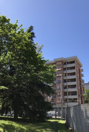 Un edificio residencial de varios pisos con balcones y un árbol grande al frente.
