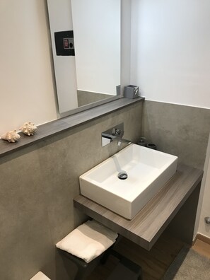Un baño moderno con un lavabo rectangular, un espejo y un perchero para toallas.