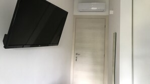 Ein Zimmer mit einem an der Wand befestigten Flachbildfernseher, einer Klimaanlage und einer geschlossenen Tür.