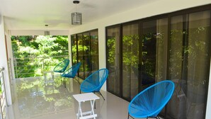 A modern balcony with large glass doors, blue chairs, and a small white table. - Casa Brillasol Samara (Sámara)