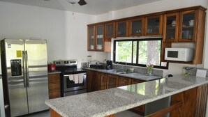 A modern kitchen with granite countertops, stainless steel appliances, wooden cabinets, and a large window providing natural light. - Casa Brillasol Samara (Sámara)