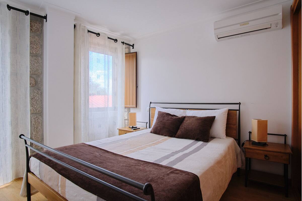 Een slaapkamer met een bed, nachtkastjes, een airconditioning en een raam met gordijnen.