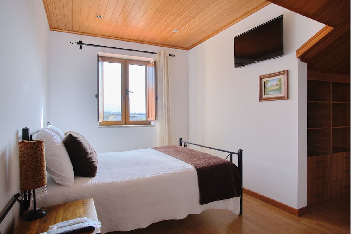 Een slaapkamer met een bed, een raam, een televisie en een houten plafond.