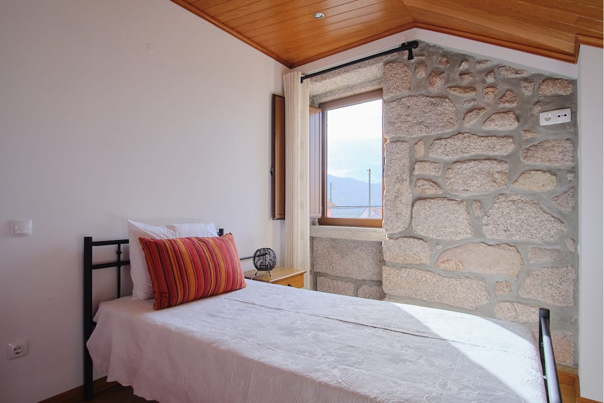 Een slaapkamer met een bed, een raam, een stenen muur en een houten plafond.