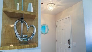 A bathroom with a heart-shaped mirror, a white door, and a chandelier.